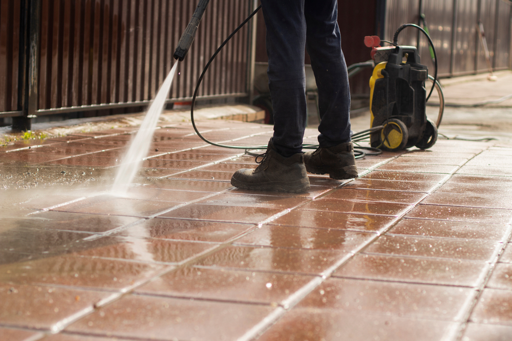 person with boots and jeans power washing outdoor concrete